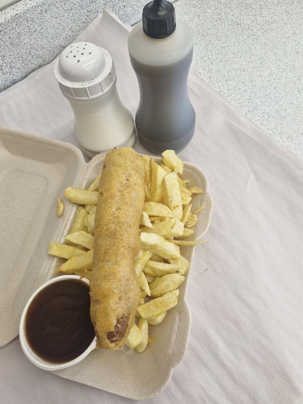 Bigfoot battered sausage on a tray of chips with a pot of gravy